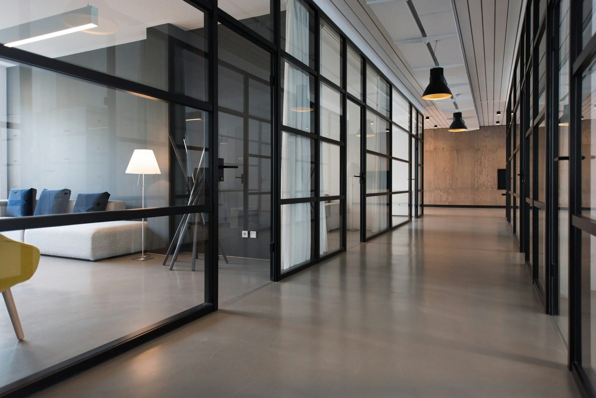 A clean, modern office hallway with reflective polished concrete floors and black-framed glass walls, demonstrating a high standard of commercial cleaning.