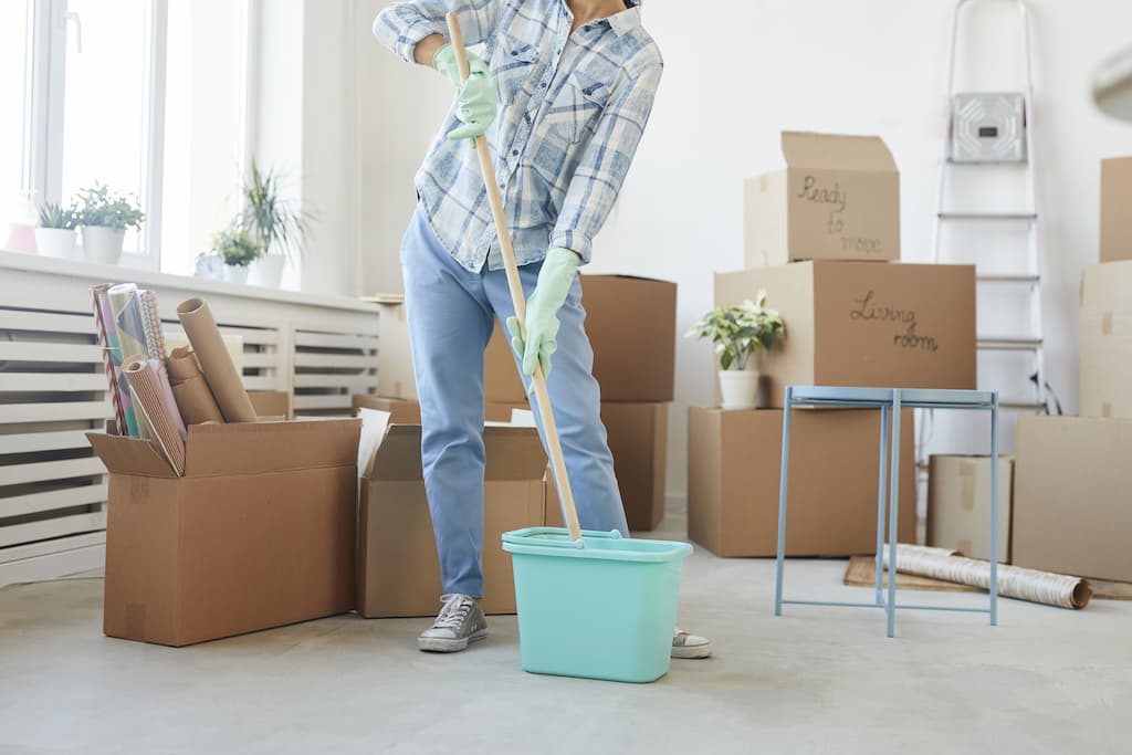 A person in gloves mopping the floor of an empty room surrounded by cardboard moving boxes, indicating a move-in or move-out cleaning service.
